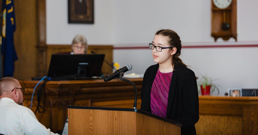 Girl with glasses on the witness stand during a Mock Trial event.