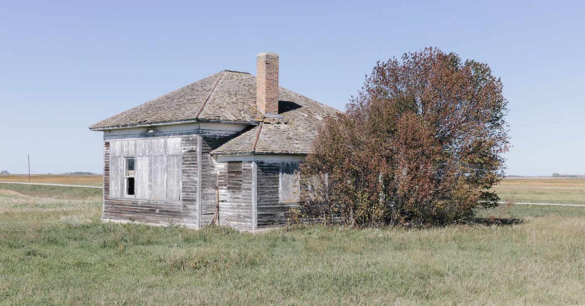 One room school house building by a road on the prairie.