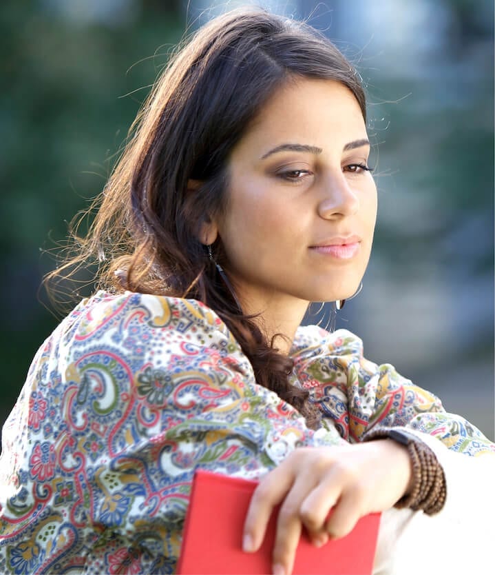 a young woman holding a red notebook staring out of frame deep in thought