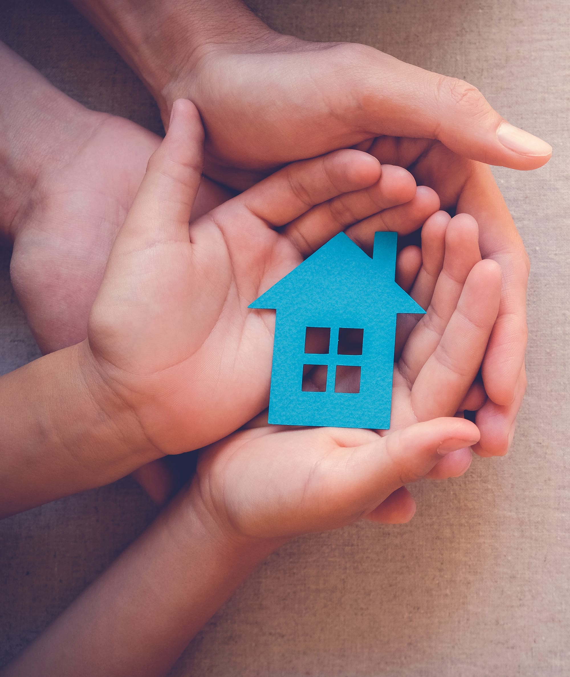 two open faced hands holding a blue paper cutout in the shape of a house