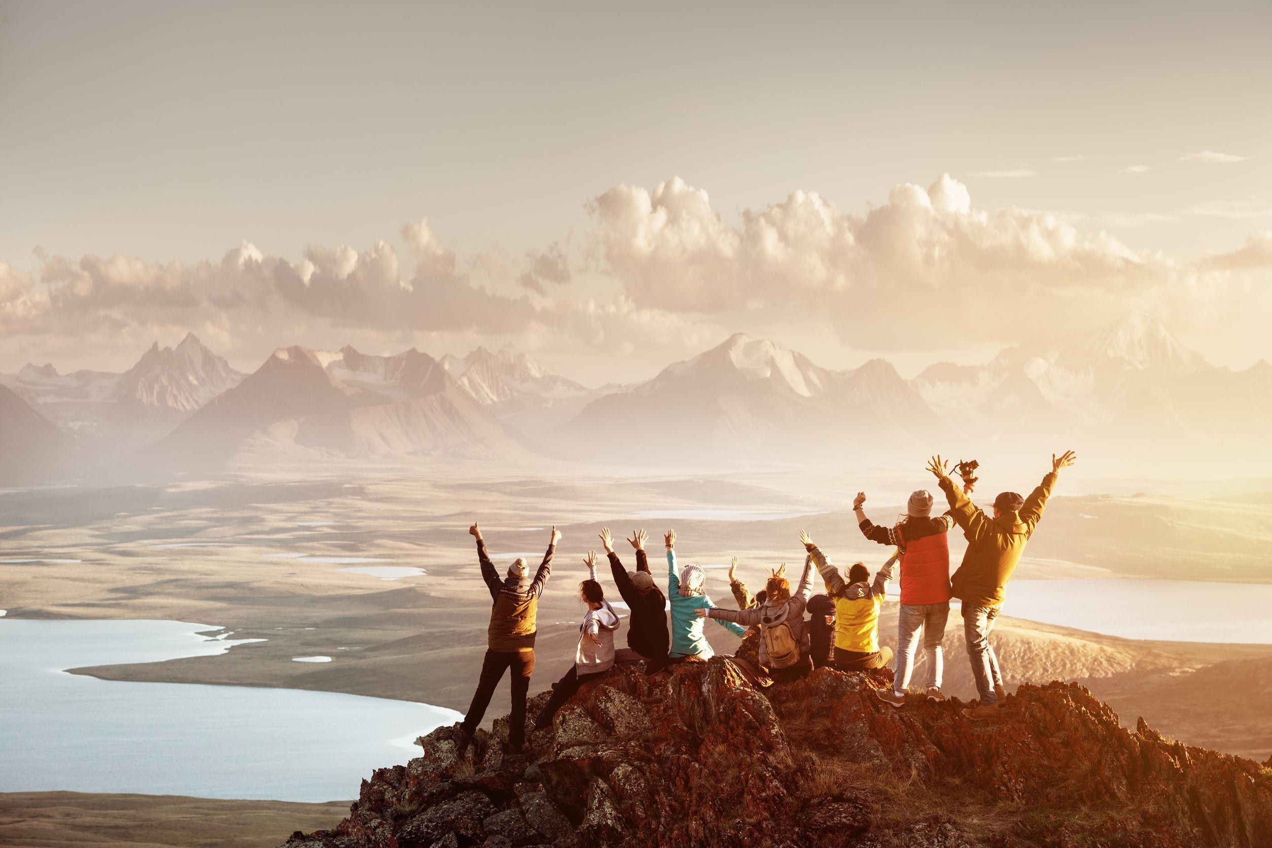 people raise their arms in celebration on top of a mountain peak