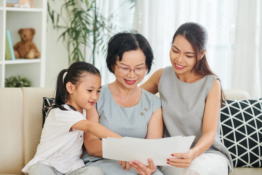Happy Asian family of three sitting on sofa with sheets of papers and reading letters together in the living room at home
