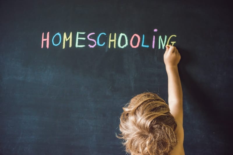 a student writes the word 'homeschooling' on a chalkboard