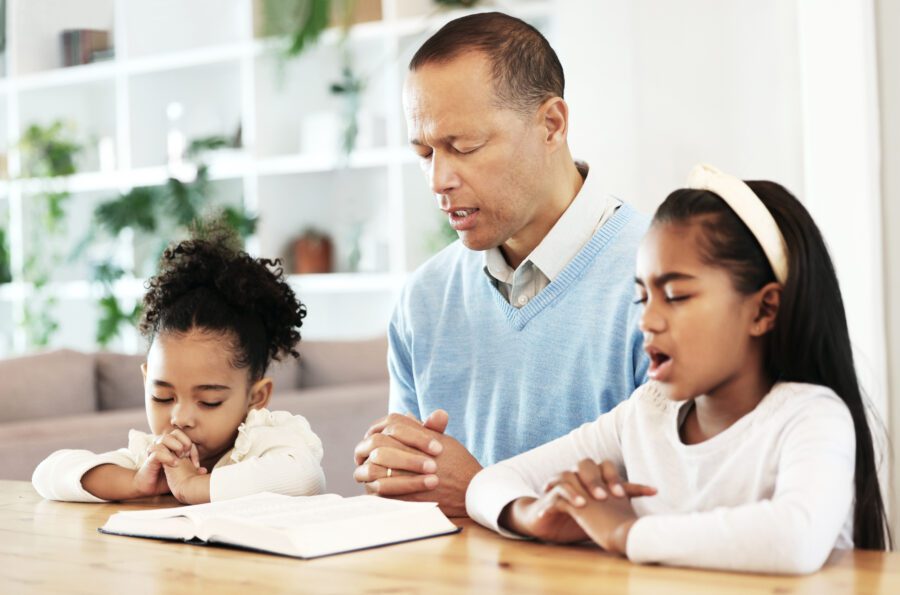 Family; worship and Bible with father and kids praying at table.