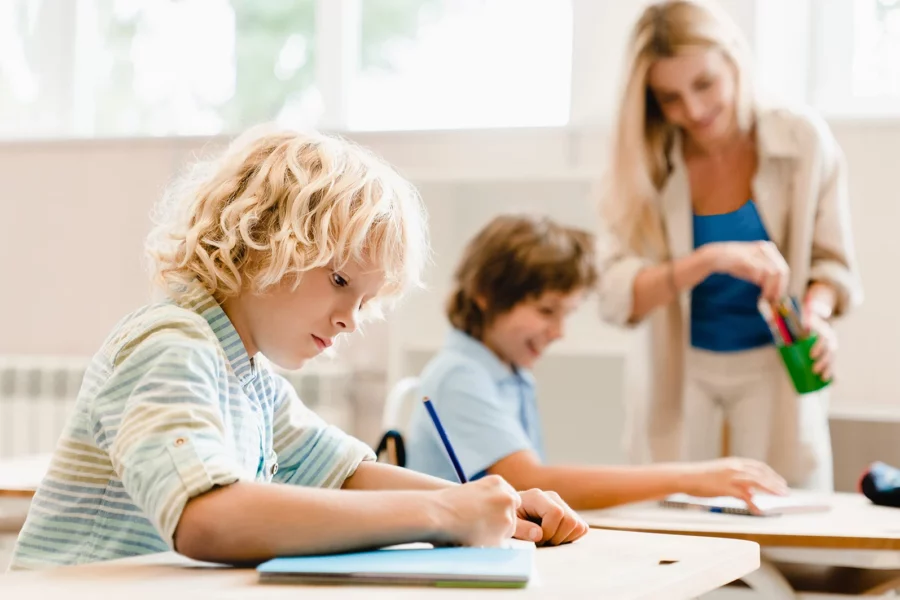 Two children working at desks with mother helping