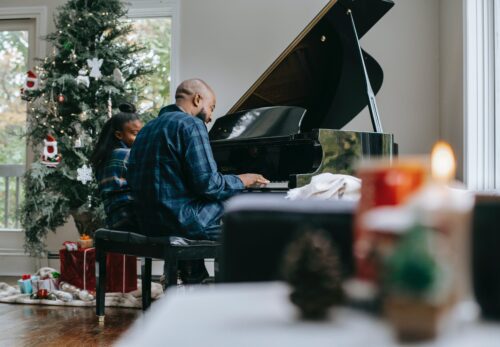 A father and a daughter play the piano and sing Christmas carols together.