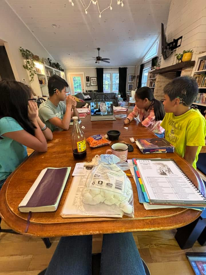 A homeschool family at the kitchen table watching a video.