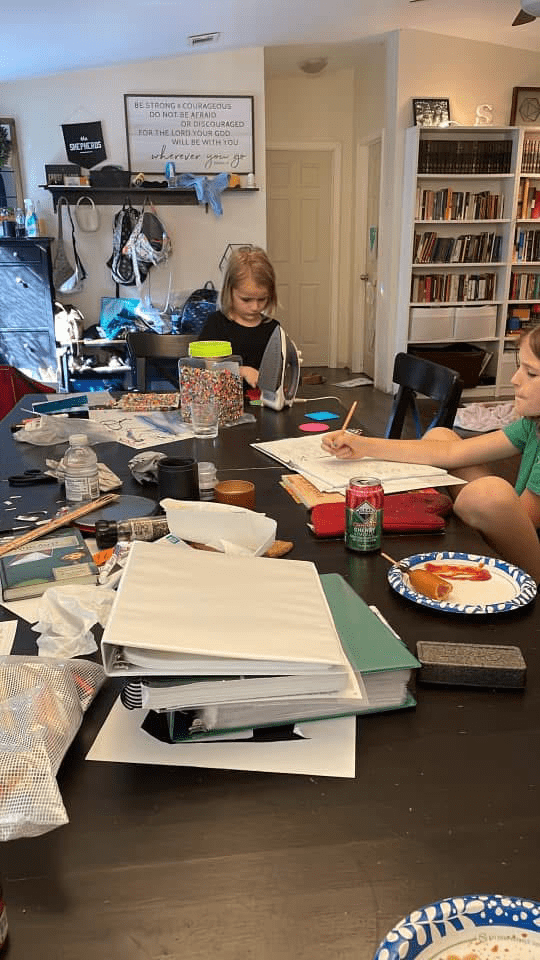 Homeschool kids with stacks of papers and books on the kitchen table.