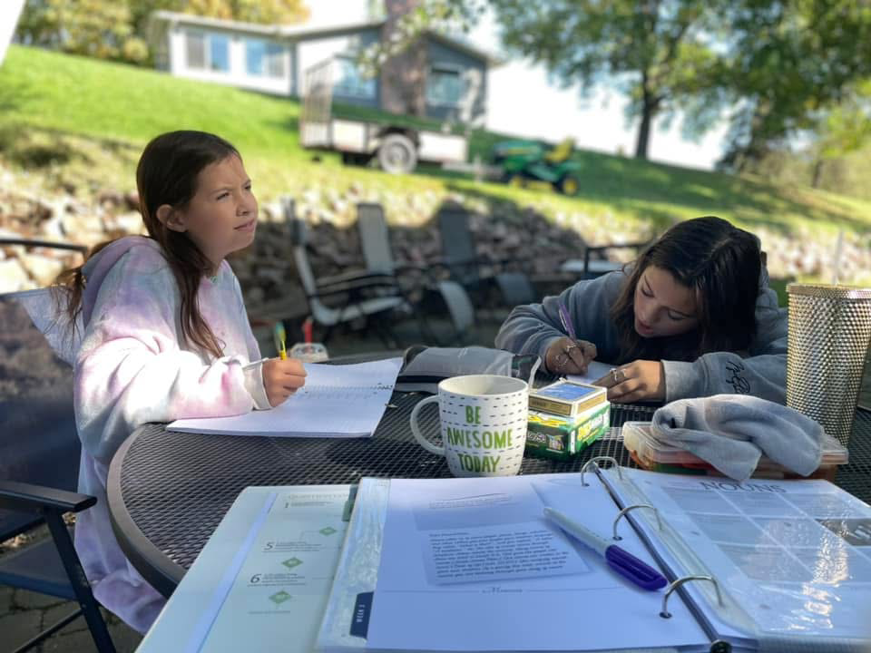 Two girls enjoying homeschooling outside at the backyard table.