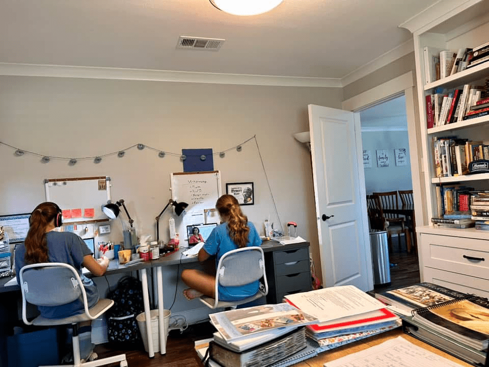 Two girls at desks, facing computers, doing homeschool work.