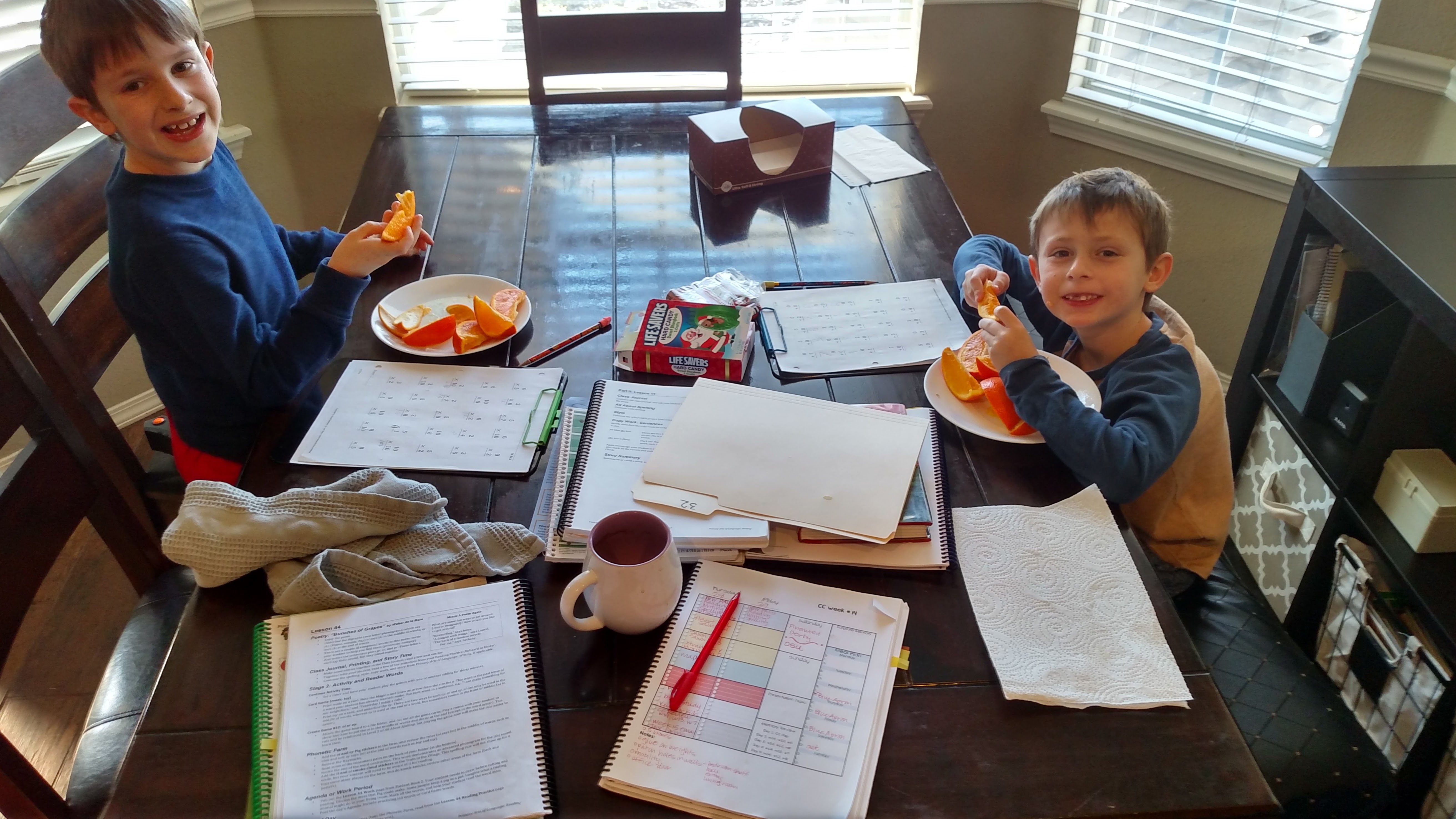 Two young boys snacking and doing homeschool at the kitchen table.