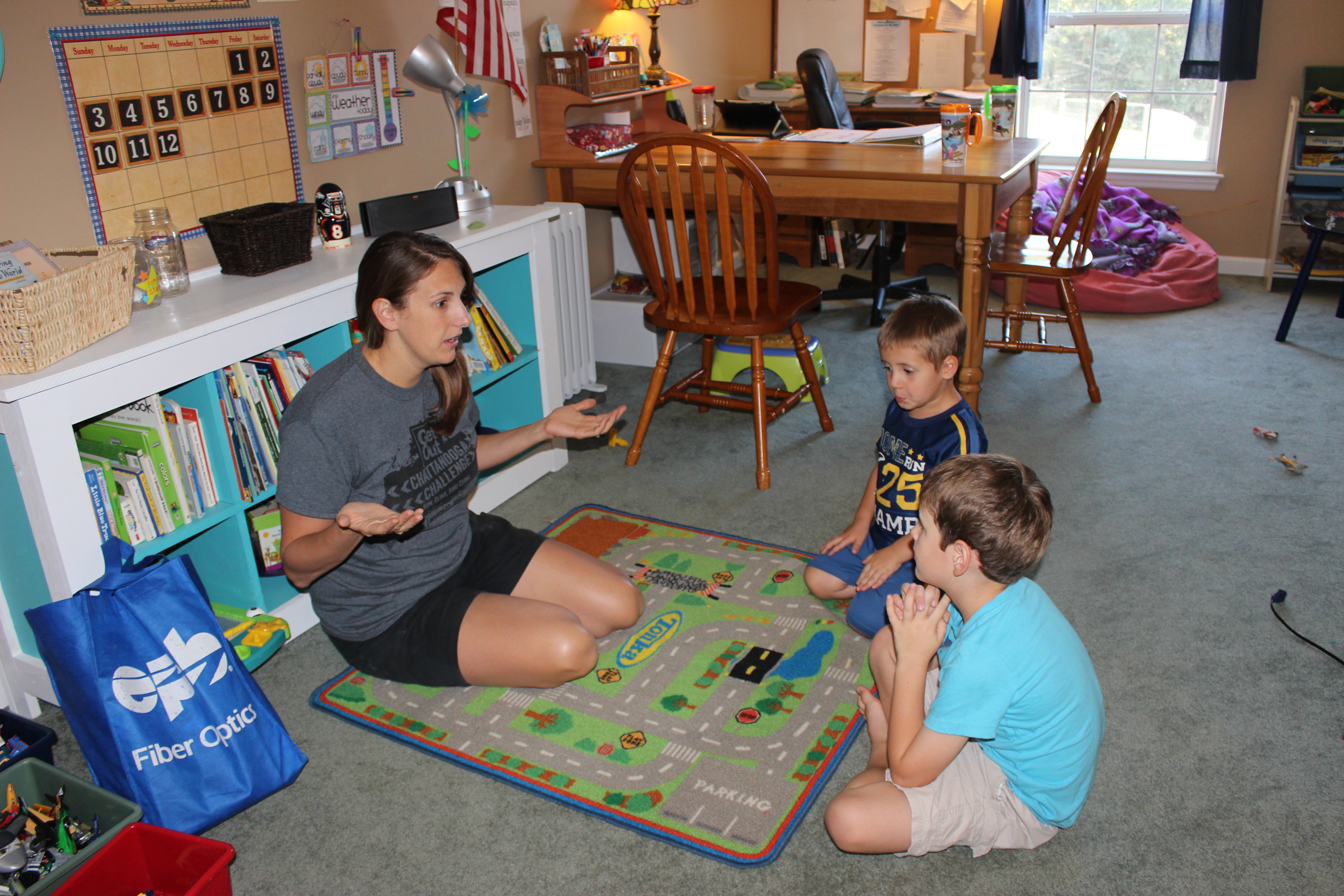 Mom and two sons homeschooling on a colorful carpet.