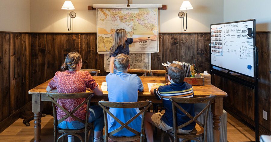 Family homeschooling at the dining room table and mom teaching from a map.