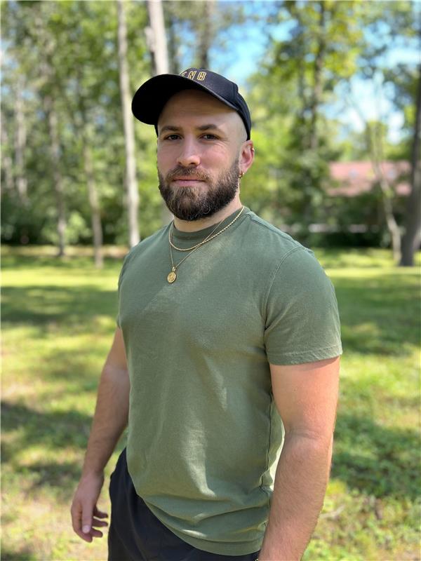 Man with green shirt and hat standing in a park.